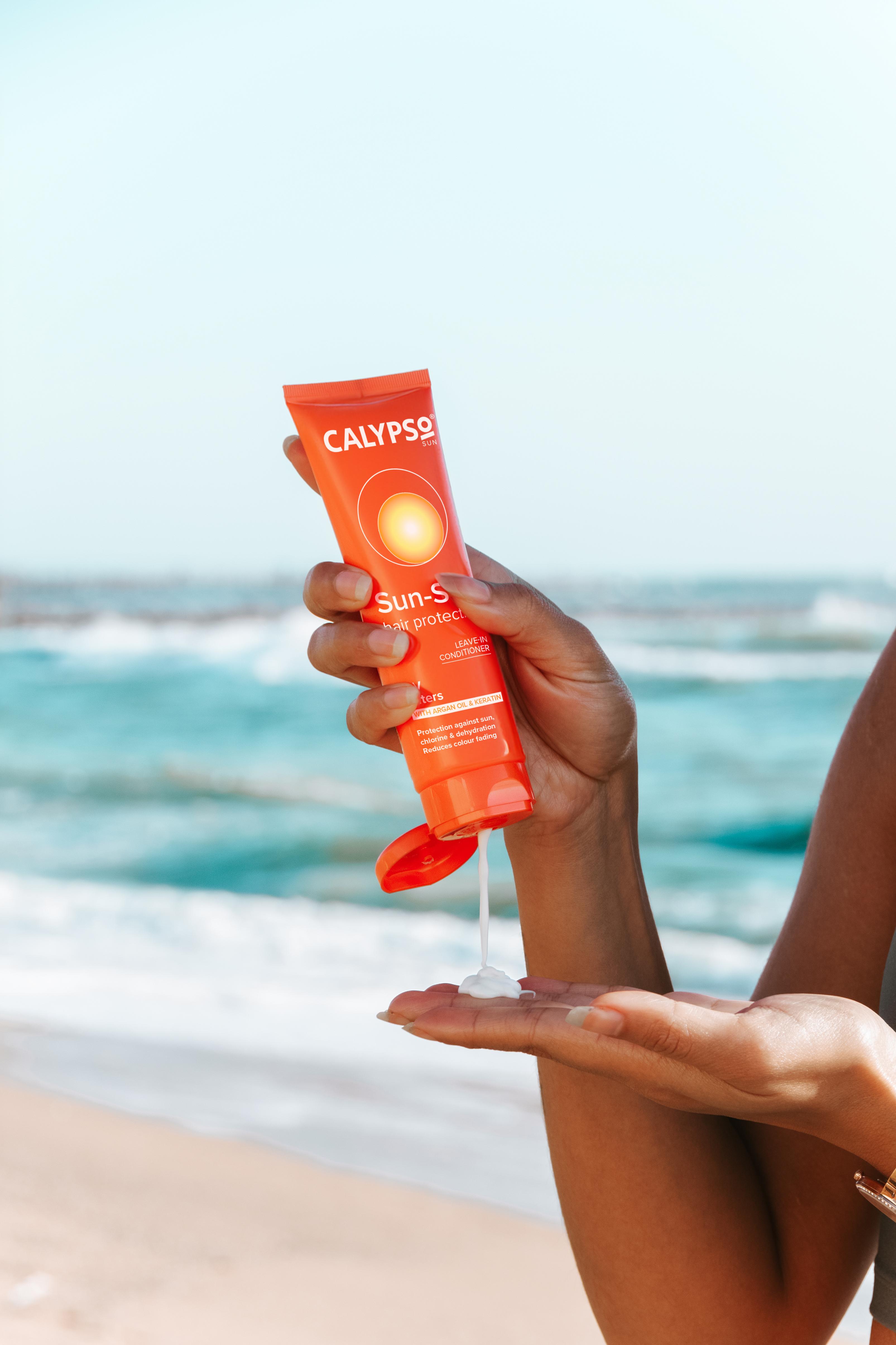 Squeezing a tube of Calypso Sun Sea Hair Protection on a beach